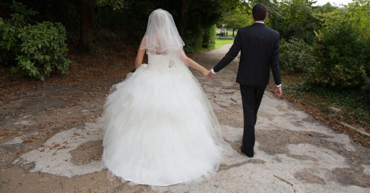 A bride and groom walk away from the camera at an outdoor wedding