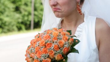 A bride has an angry expression and holds a bouquet with orange flowers