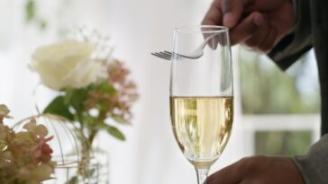 Shot of an unrecognizable man tapping a fork against a champagne glass to make an announcement.