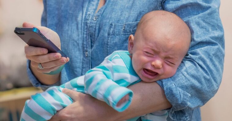 Woman texting and holding crying baby boy