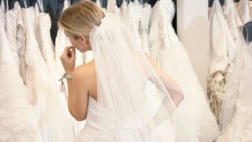 Back view of a young woman in wedding dress looking at bridal gowns on display in boutique.