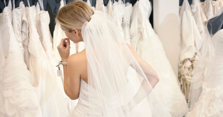 Back view of a young woman in wedding dress looking at bridal gowns on display in boutique.