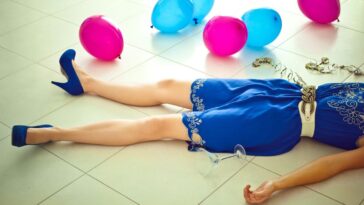 Woman lying down on the floor with balloons and wine glass.