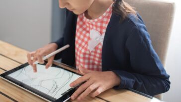 A young girl draws on a tablet with a digital pen in her living room