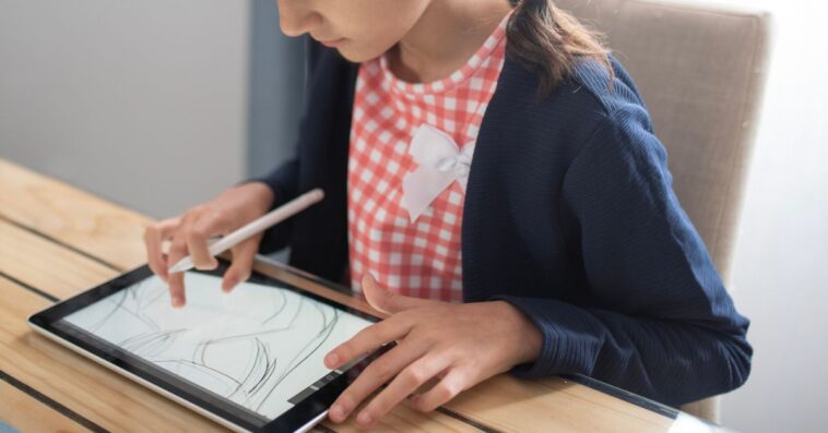 A young girl draws on a tablet with a digital pen in her living room