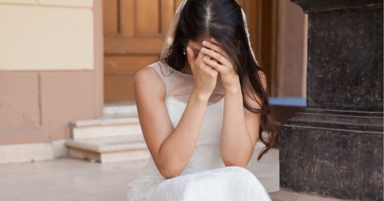 A bride sits on church steps, sad with her head in her hands