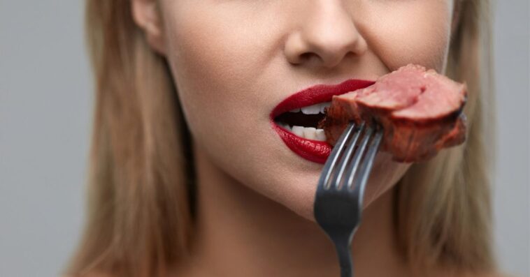 Woman Eating Meat. Closeup Of Beautiful Female Face Biting Meat