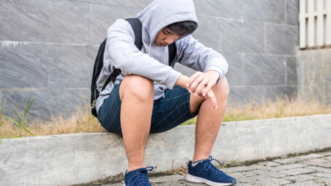 Sad teenage boy sitting on the sidewalk.