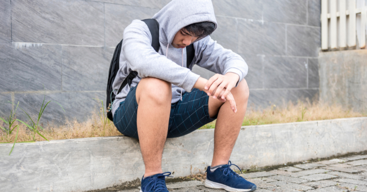 Sad teenage boy sitting on the sidewalk.
