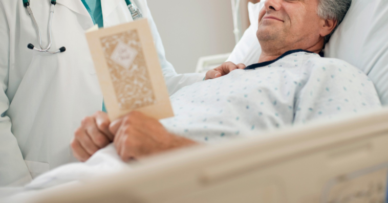 man in hospital bed looks at Get Well card with doctor
