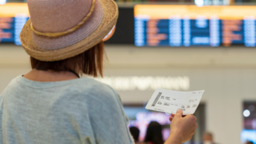 woman holding plane ticket looking at departure board in airport
