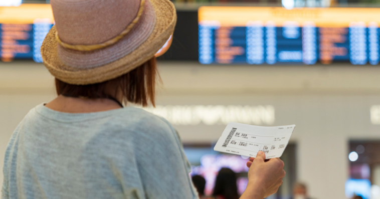 woman holding plane ticket looking at departure board in airport