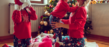 mother with two children in Christmas pajamas with toys in front of a tree