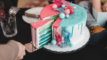 Woman cutting into blue cake with blue and pink icing at a gender reveal party.