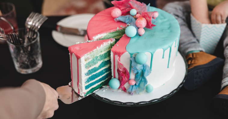 Woman cutting into blue cake with blue and pink icing at a gender reveal party.