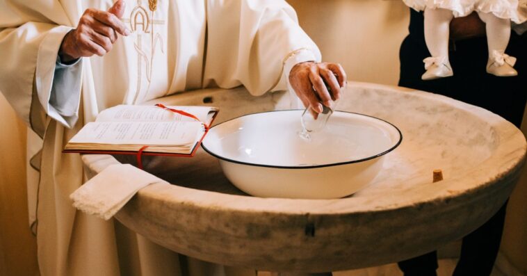 A priest pours the sacred water into the baptismal font during a baby's baptism