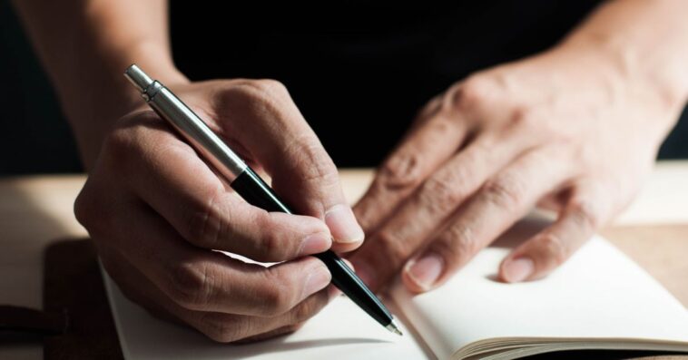 A close-up view of a man writing on a notepad