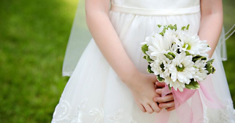 Close-up of a Little Girl in a First Communion or white Flower Girl Dress without her face, holding white and green flowers