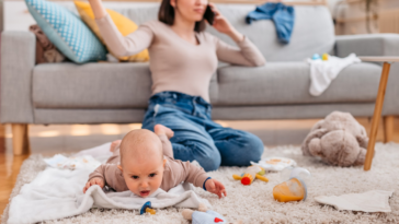 mother speaking on phone while baby plays on floor