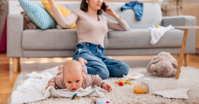 mother speaking on phone while baby plays on floor