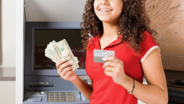 teen girl in front of ATM holding money and a debit card
