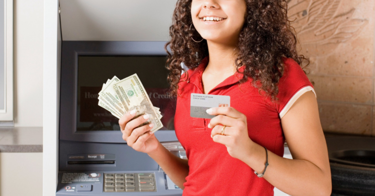 teen girl in front of ATM holding money and a debit card