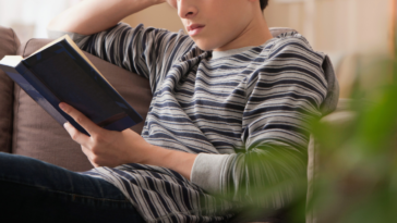 teenage boy seated on couch reading a book