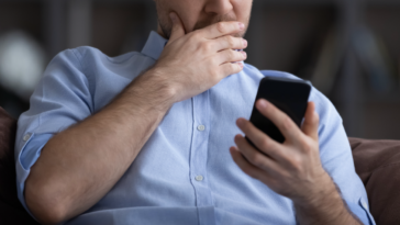 Man looking at his phone with his hand covering his mouth.