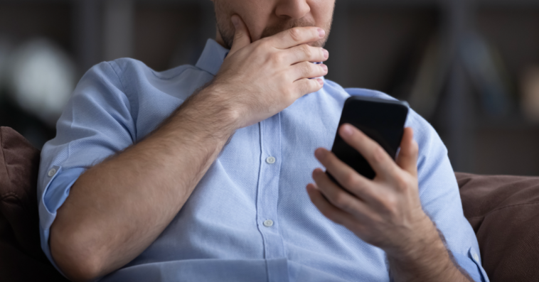 Man looking at his phone with his hand covering his mouth.