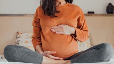 Cropped Pregnant woman, sitting in crossed legs in be at home holding her belly