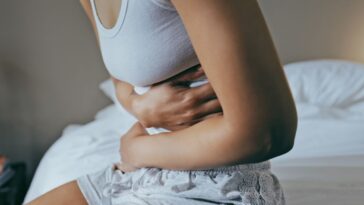 Stomach ache and hands of woman on her belly, in bedroom, for indigestion, cramps and illness.