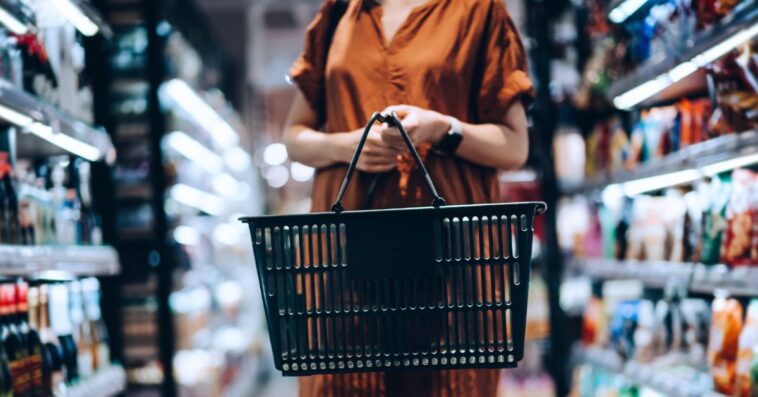 Cropped shot of young woman carrying a shopping basket, standing along the product aisle