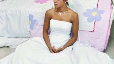 crying bride in wedding dress sitting on floor by childhood bed
