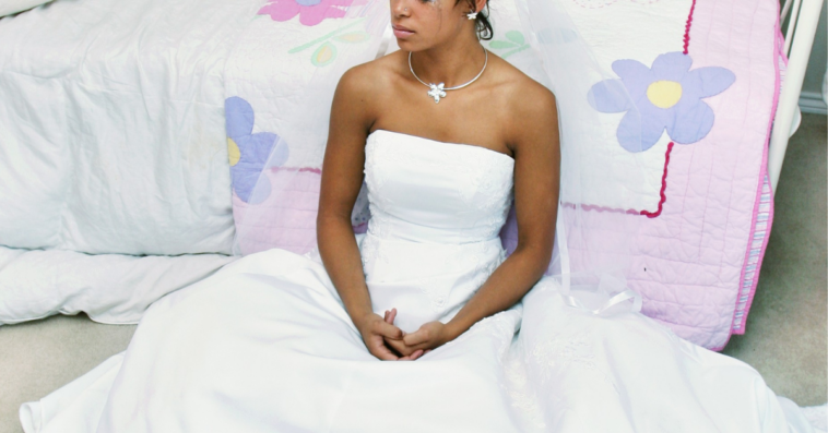 crying bride in wedding dress sitting on floor by childhood bed