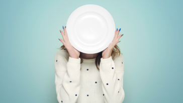 Woman hiding her face behind a plate.