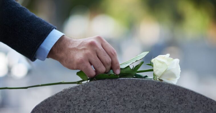 Cropped shot of a man placing a white rose on a grave