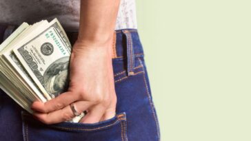 A woman stuffs hundreds of dollars into the back of her jeans
