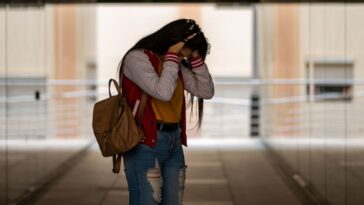 Side view of an angry teen girl in casual clothing with backpack standing alone in a corridor