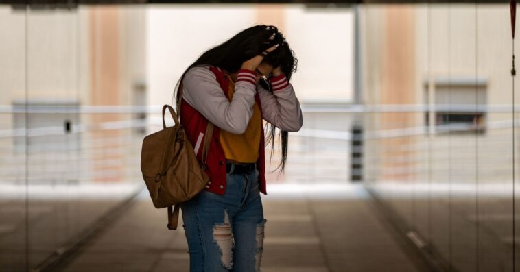 Side view of an angry teen girl in casual clothing with backpack standing alone in a corridor