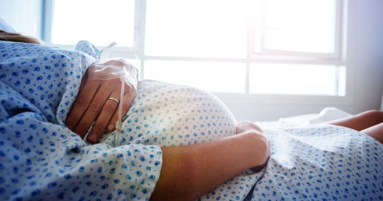 Close-up of a pregnant woman's belly in a hospital bed with a catheter in her hand