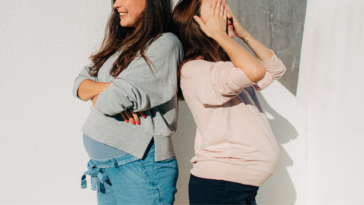two pregnant women stand back to back
