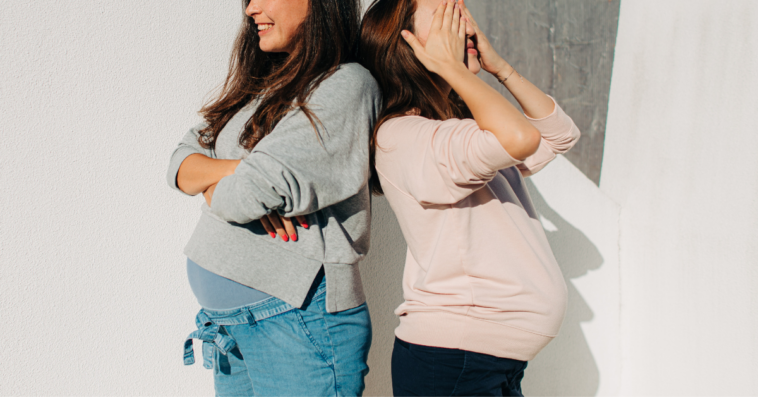 two pregnant women stand back to back