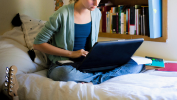 young woman using laptop on bed in college dorm