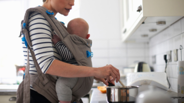 woman cooking with infant in sling
