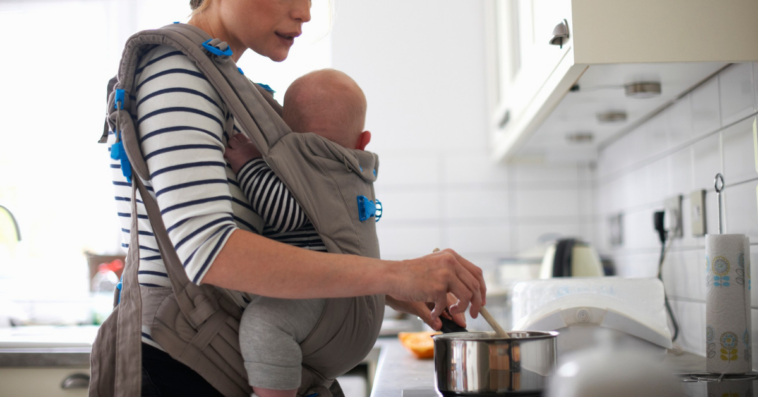 woman cooking with infant in sling