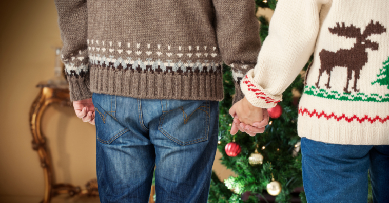 Gay couple holding hands wearing Christmas sweaters.