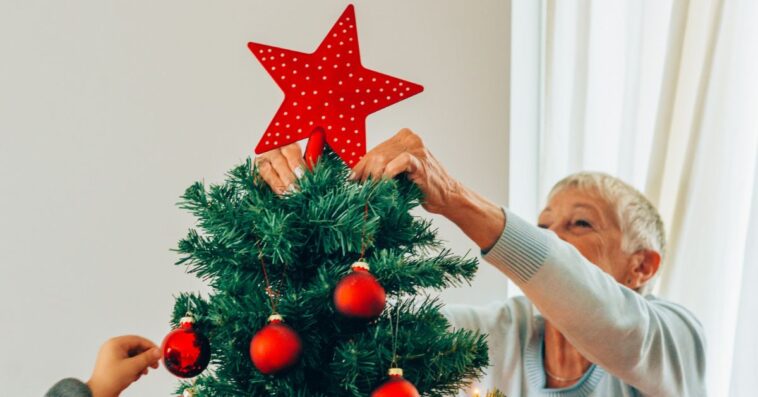 Beautiful senior woman putting the Christmas star on top of the Christmas tree.