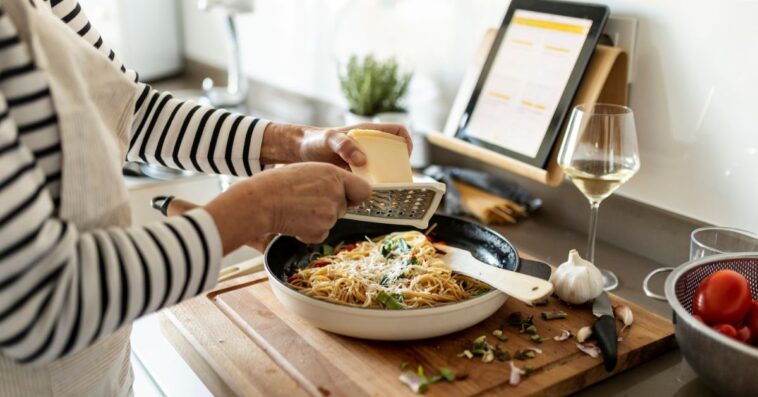 Close-up of woman with tablet cooking pasta dish in kitchen at home