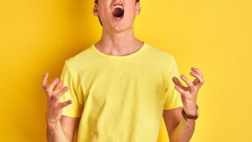 Teenager boy wearing yellow t-shirt over isolated background crazy and mad shouting and yelling with aggressive expression and arms raised.