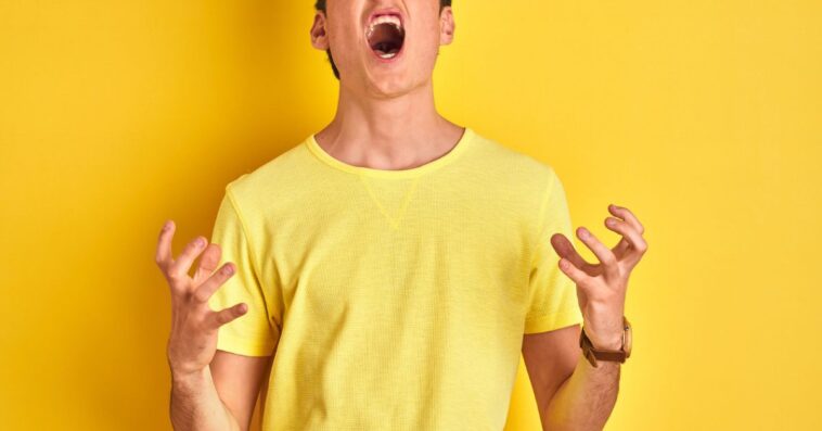 Teenager boy wearing yellow t-shirt over isolated background crazy and mad shouting and yelling with aggressive expression and arms raised.